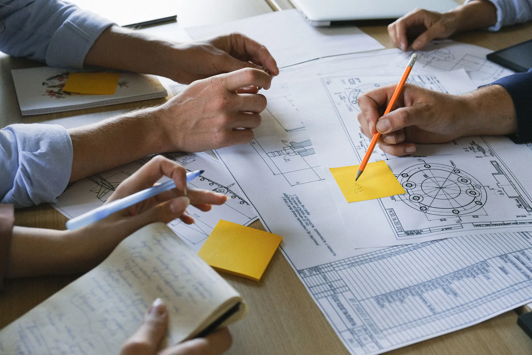 Hände eines Teams über technischen Zeichnungen auf einem großen Arbeitstisch